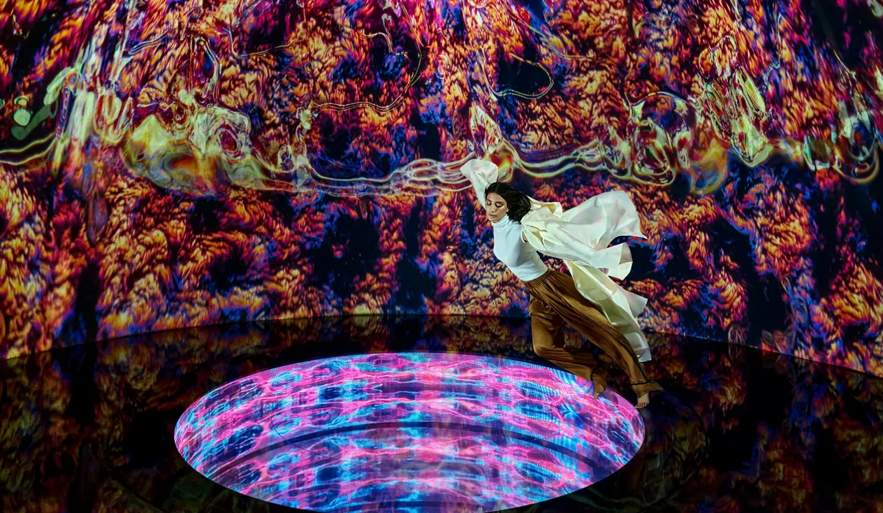 A dancer in flowing attire leaps gracefully over a vibrant, illuminated circular platform, surrounded by abstract colorful...