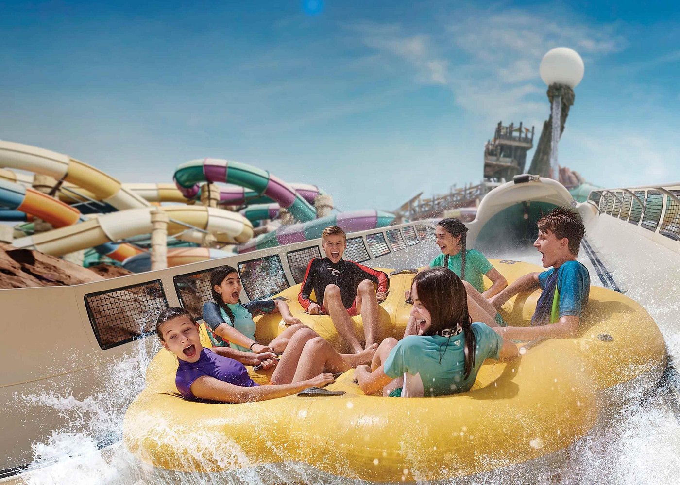 A group of excited kids enjoy a thrilling water slide ride in a yellow raft, splashing through water at a vibrant water park.
